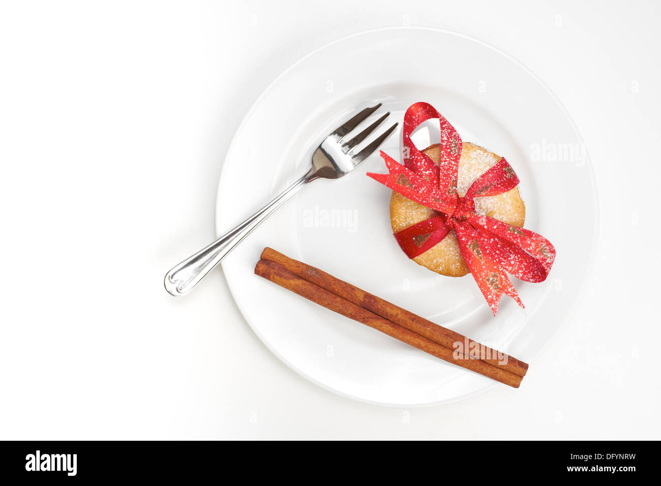 Noël sucré émincer pieand le bâton de cannelle avec un ruban rouge attaché autour sur une assiette blanche et l'arrière-plan. Banque D'Images