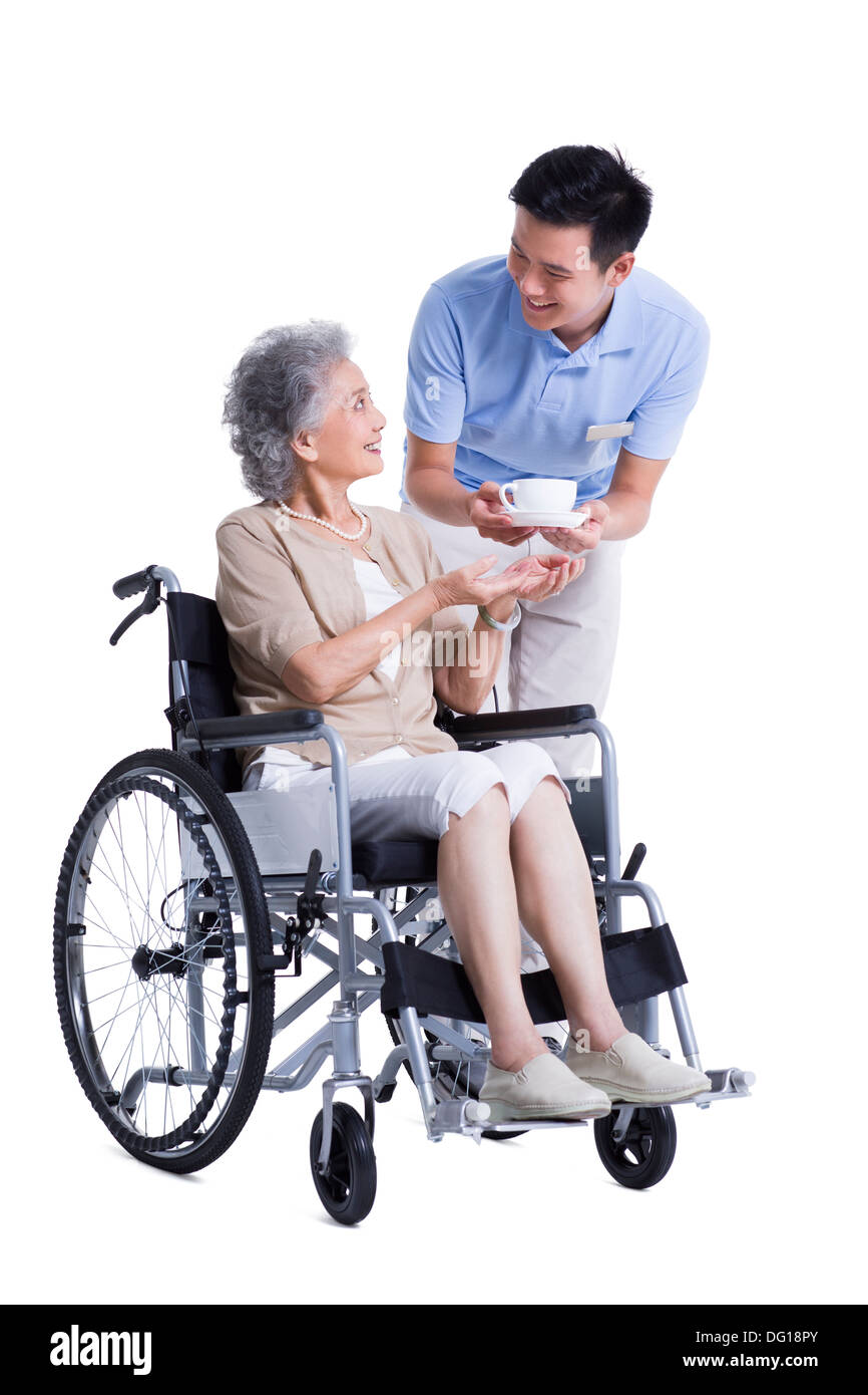 Assistant de soins infirmiers Hommes femme en fauteuil roulant remise une tasse de café Banque D'Images