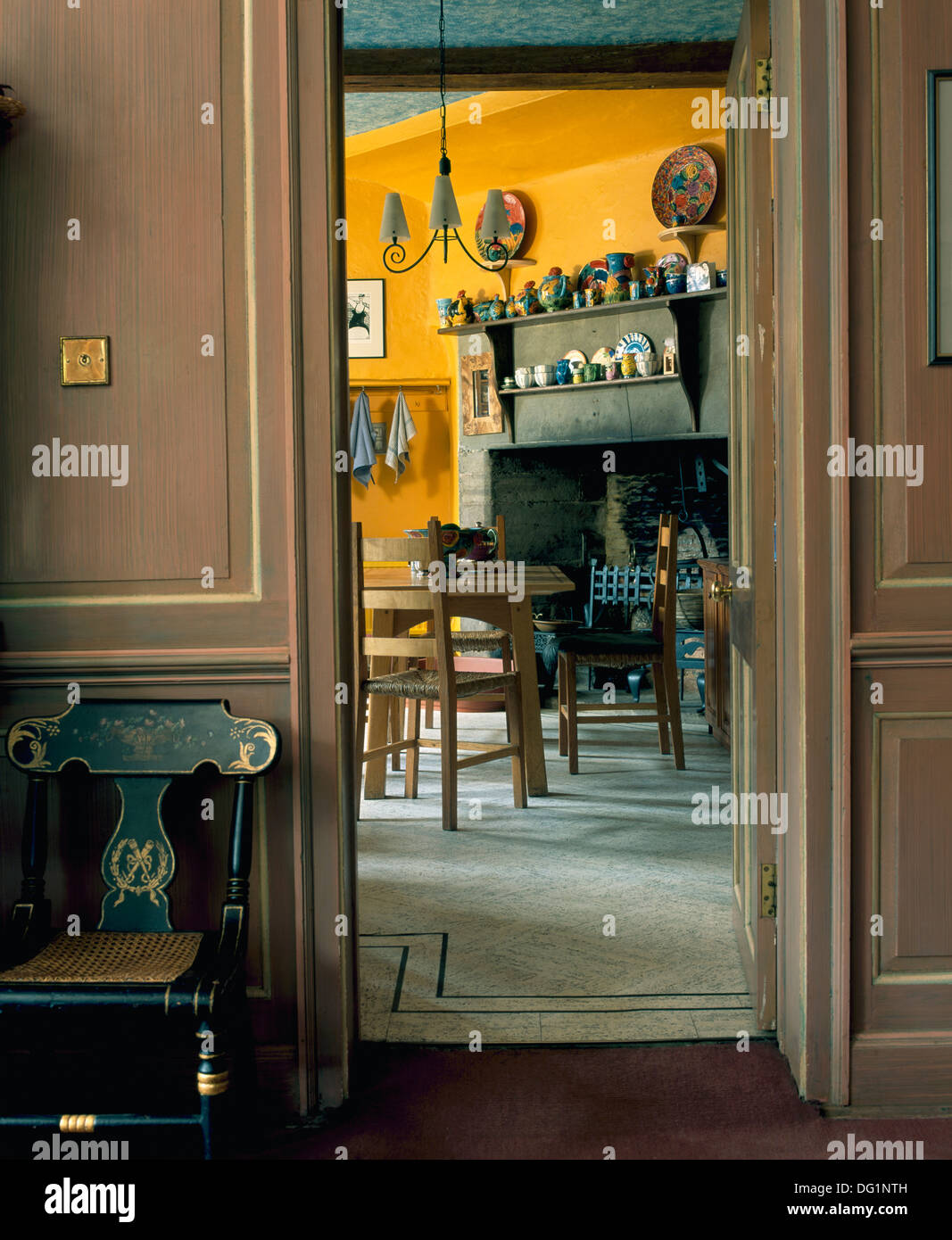 Hall lambrissé peint en gris avec des meubles incrustés chaise à côté de porte ouverte sur salle à manger pays jaune Banque D'Images