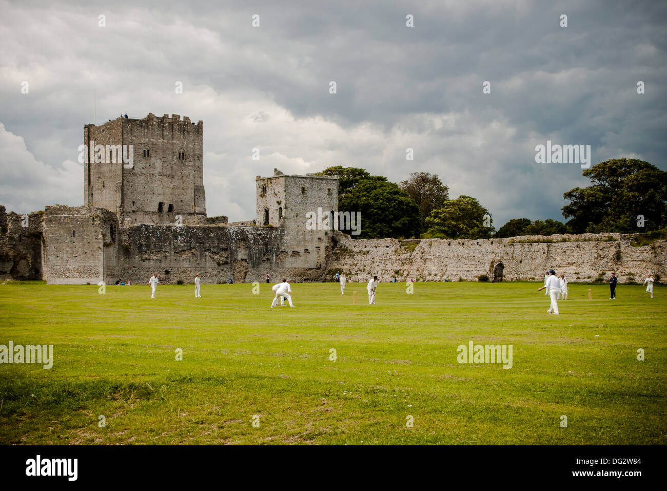 Cricketers à jouer au cricket dans le parc du château de Portchester, Hampshire sous un ciel d'orage Banque D'Images