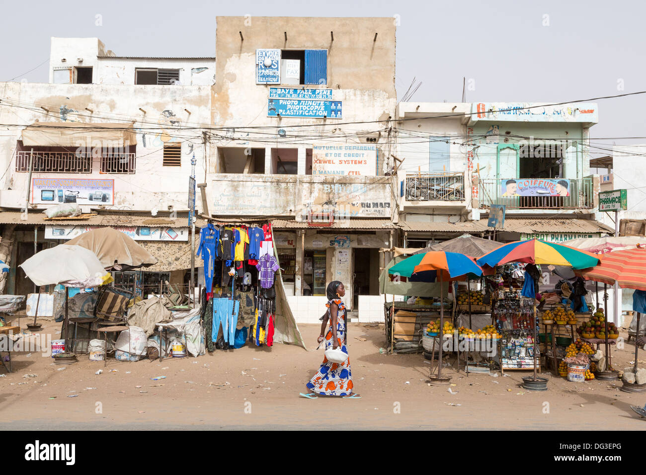 Sénégal, Touba. Scène de rue, femme marche passé des vêtements et des fruits. Banque D'Images