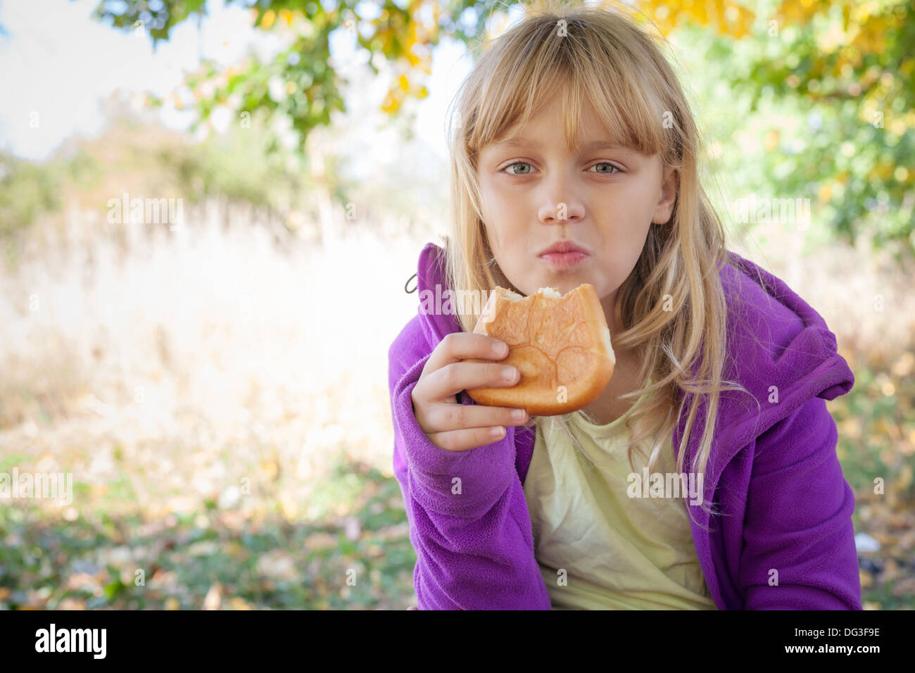 Petite blonde girl in autumn park mange petite tarte Banque D'Images