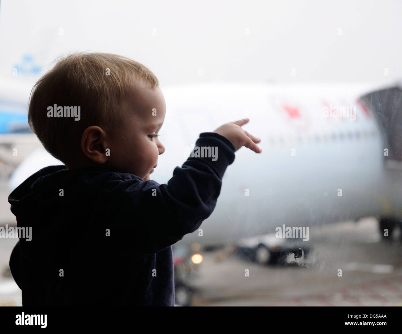 Un jeune garçon à la fenêtre par un aéroport à l'extérieur des avions Banque D'Images