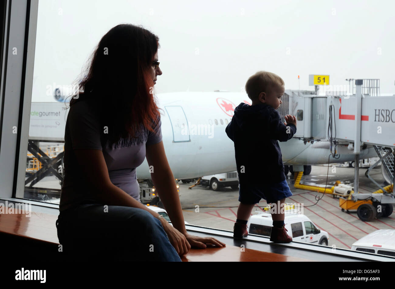 Un jeune garçon et sa mère à la fenêtre par un aéroport à l'extérieur des avions Banque D'Images