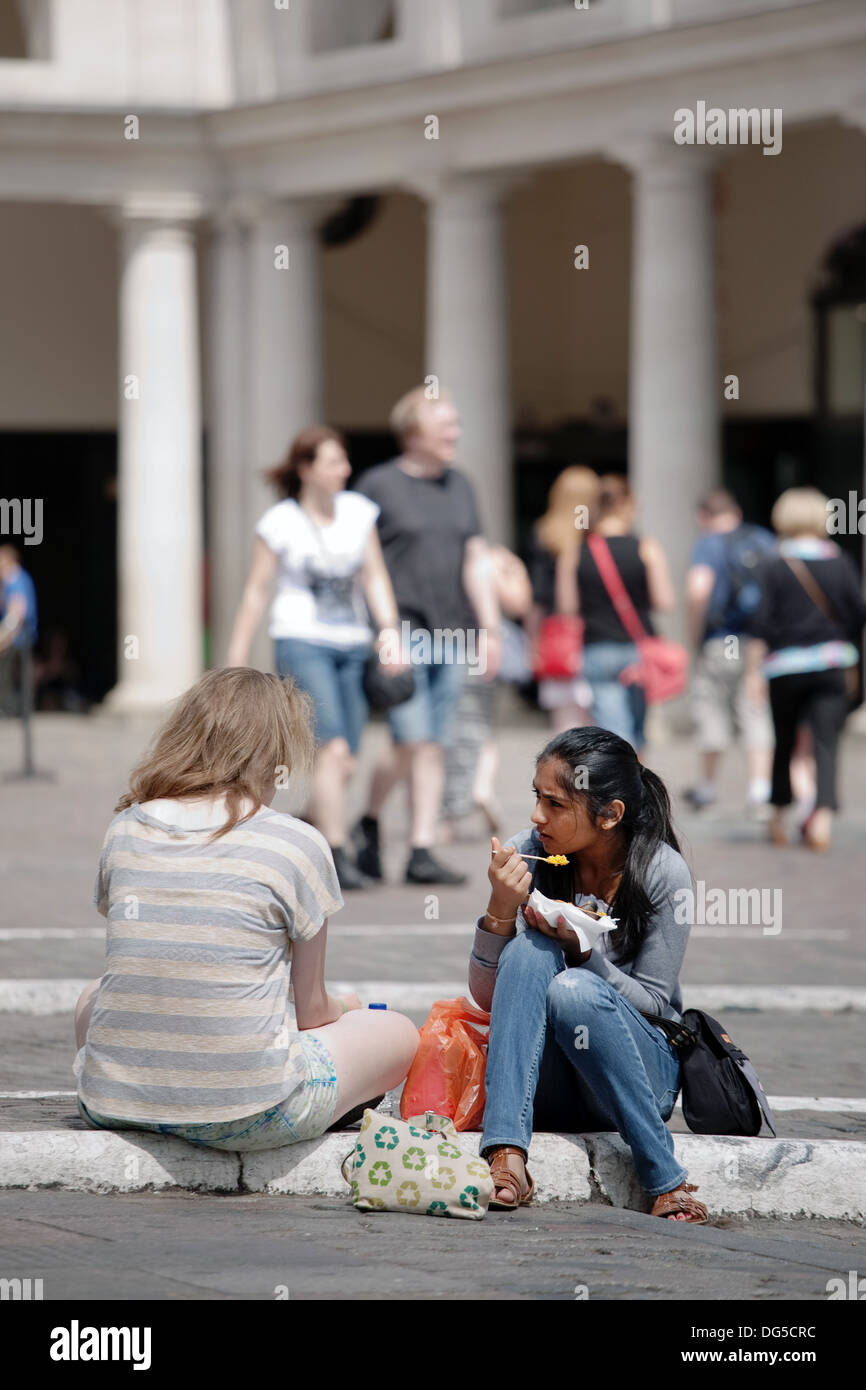 Deux jeunes femmes, une femme de race blanche et une femme asiatique - manger le déjeuner assis sur le plancher à Covent Garden à Londres Banque D'Images