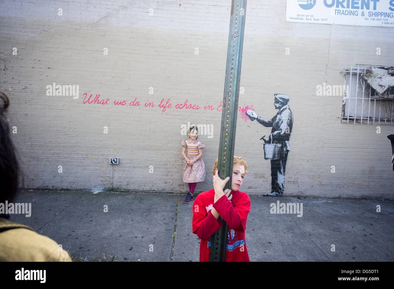 New York, USA. 14Th Oct, 2013. Les parents amènent leurs enfants à la Woodside quartier de Queens à New York le lundi 14 octobre, 2013 pour voir la quatorzième tranche de l'art graffiti de Banksy, 'ce que nous faisons dans la vie résonne dans l'éternité". L'insaisissable artiste de rue, c'est la création d'œuvres autour de la ville chaque jour durant le mois d'octobre, accompagnée d'un message enregistré, vous pouvez entendre en appelant le numéro 1-800-656-4271 suivi de #  et le nombre d'œuvres. (© Richard B. Levine) Crédit : Richard Levine/Alamy Live News Banque D'Images