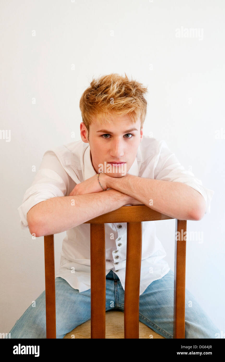 Jeune homme assis à califourchon sur la chaise, s'appuyant sur le dos et regardant la caméra Banque D'Images