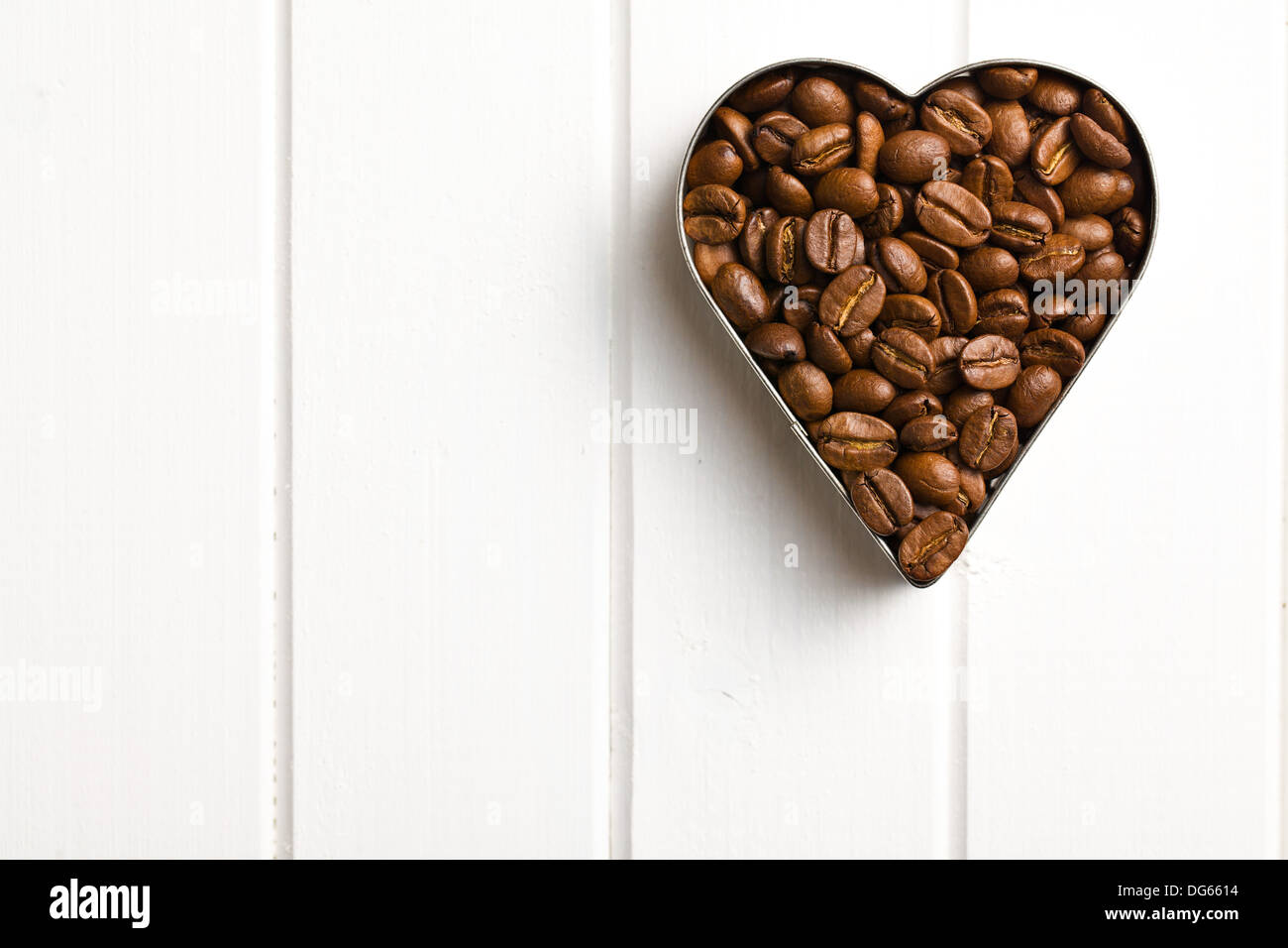 Vue de dessus de grains de café en forme coeur sur table en bois blanc Banque D'Images