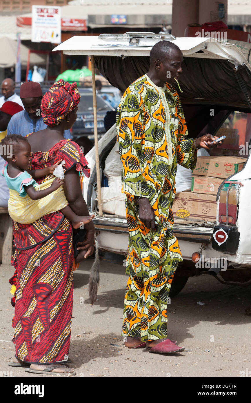 Sénégal, Saint Louis. Vêtements africains colorés à la station de bus et taxi. L'homme est à l'aide d'un stick à mâcher pour nettoyer ses dents. Banque D'Images