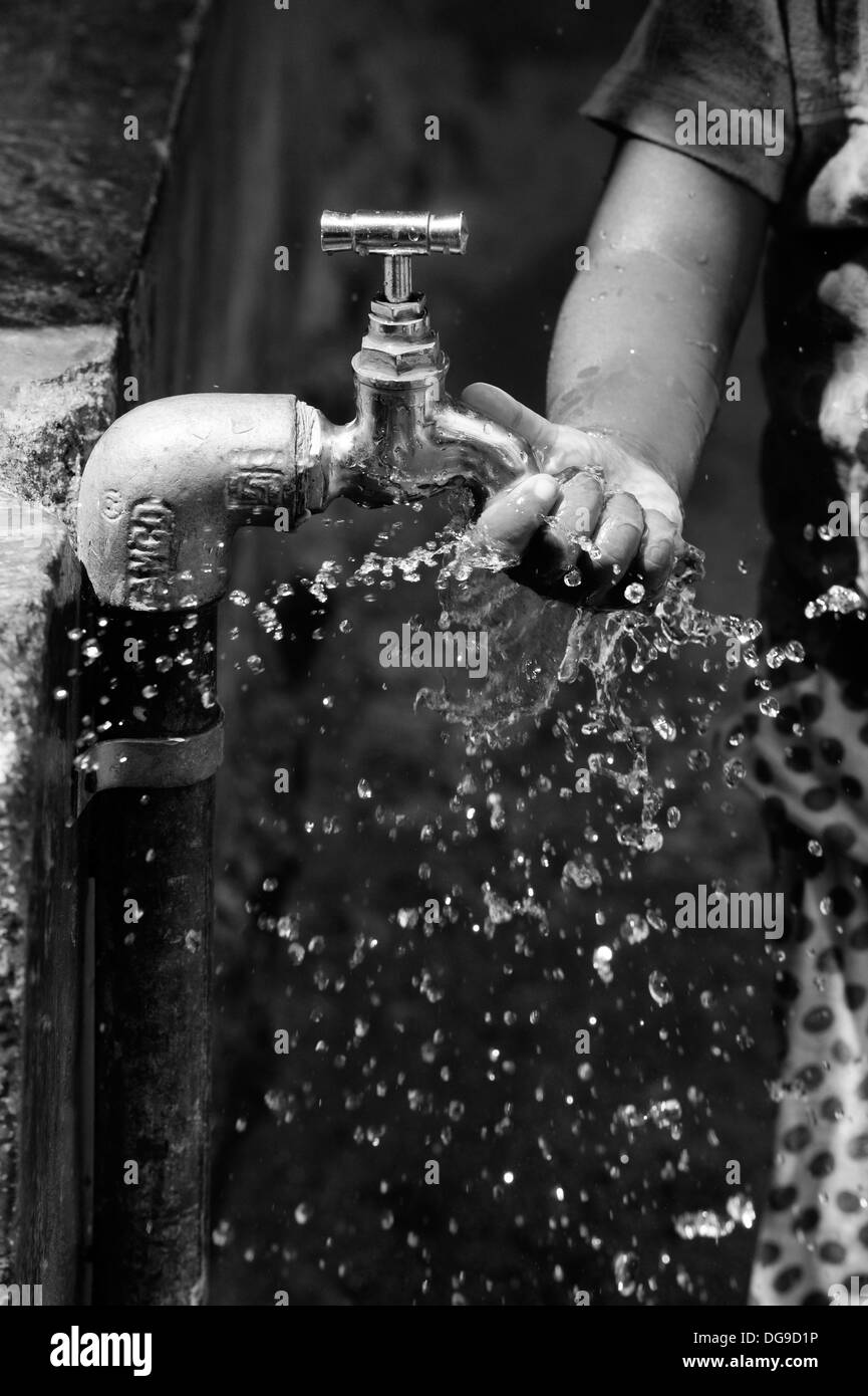 Jeune indienne / enfant jouant avec de l'eau d'un robinet dans un village de l'Inde rurale. L'Andhra Pradesh, Inde. Noir et blanc. Banque D'Images