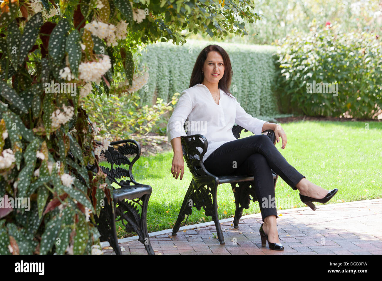 Middle aged woman sitting in cast iron chaise dans le jardin Banque D'Images