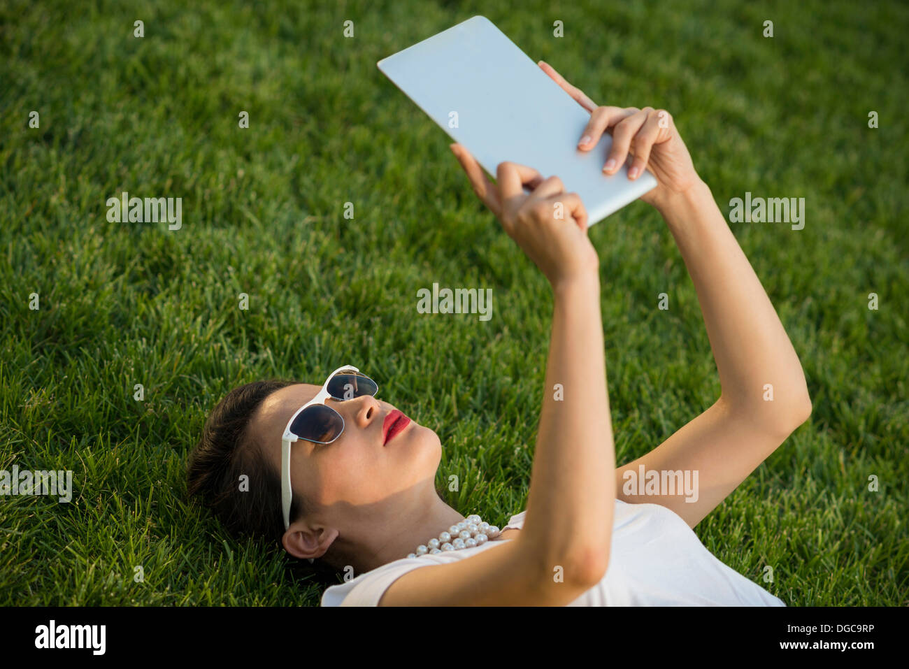 Woman lying in park using digital tablet Banque D'Images