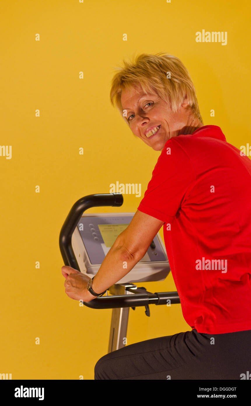 Femme dans la salle de sport, assis sur un vélo, smiling Banque D'Images