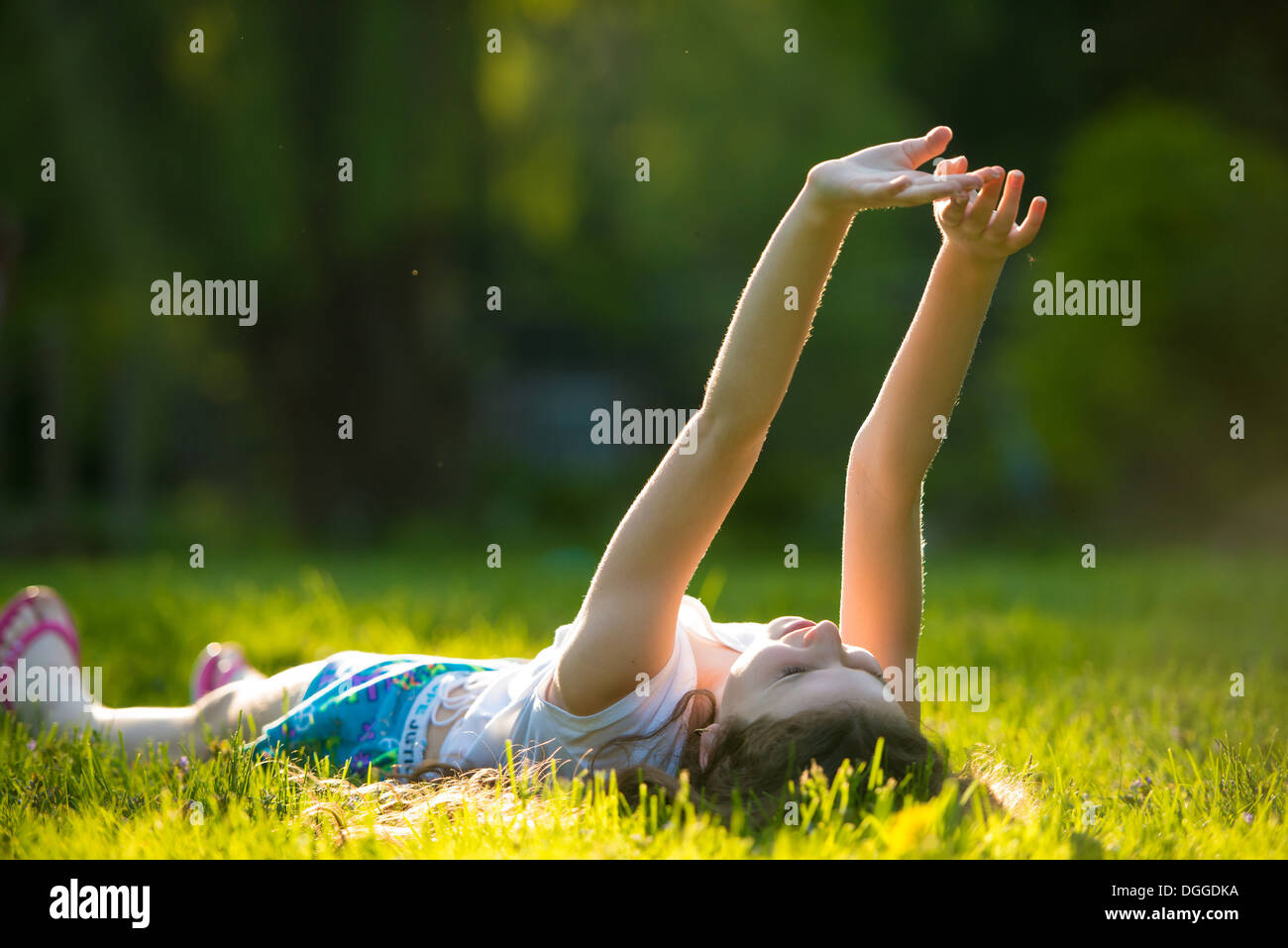Girl lying on grass with arms raised Banque D'Images