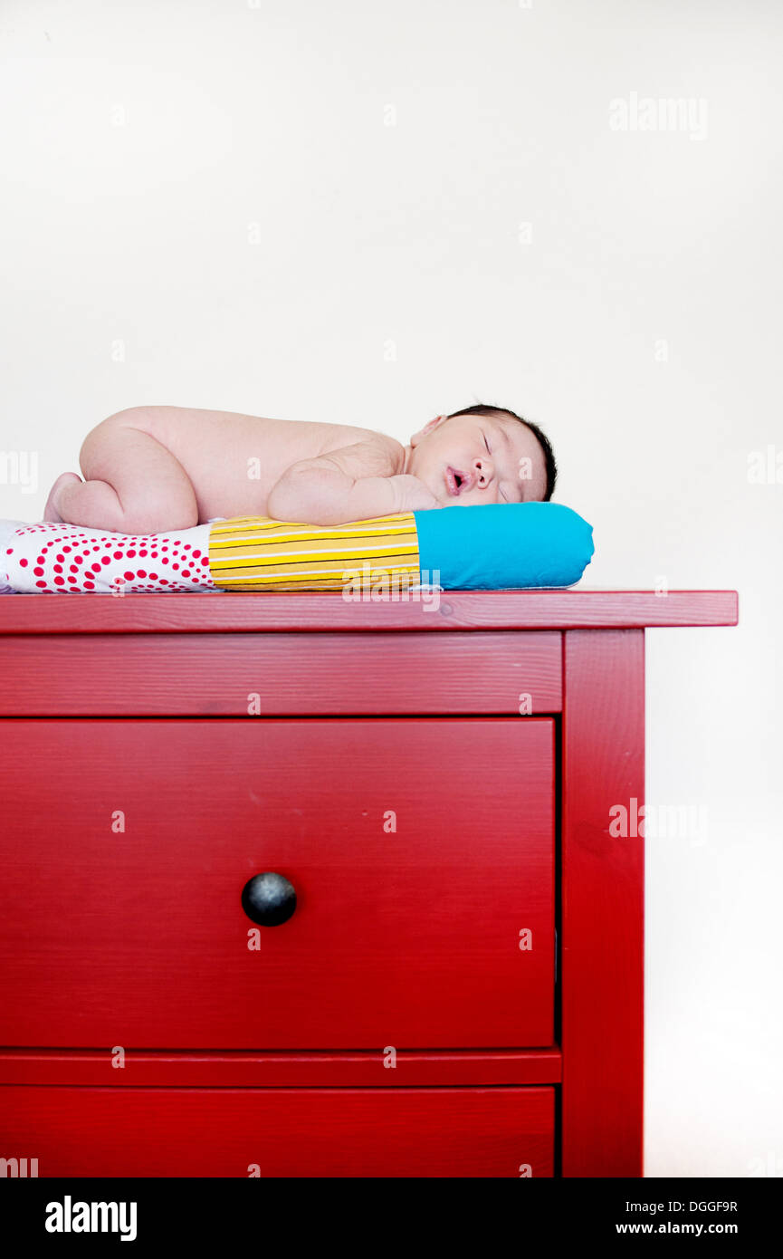 Bébé garçon endormi sur le dessus de tiroirs rouge Banque D'Images