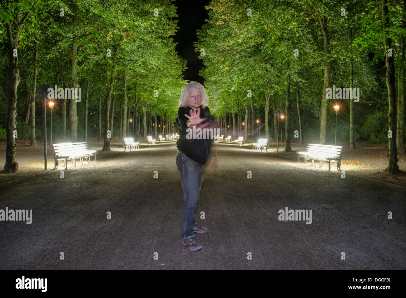 Homme debout dans une position défensive devant les rangées de bancs illiminated dans le parc Hofgarten, Duesseldorf Banque D'Images