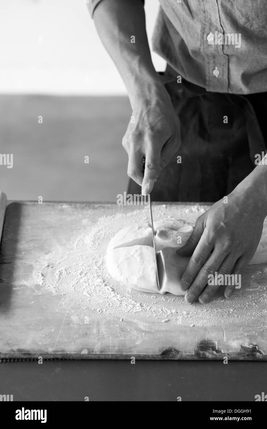 Young baker slicing pâte fraîche Banque D'Images