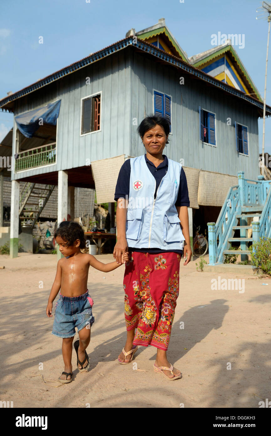 Premiers soins et agent de santé communautaire portant un gilet de la Croix-Rouge, tenant une jeune fille la main devant un traditionnel Banque D'Images