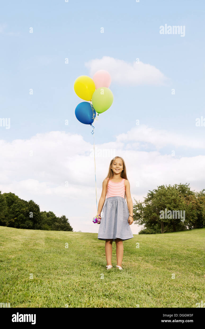 Girl holding balloons debout sur l'herbe Banque D'Images