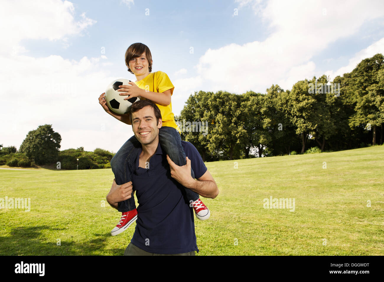 Père exerçant son fils sur les épaules avec football Banque D'Images