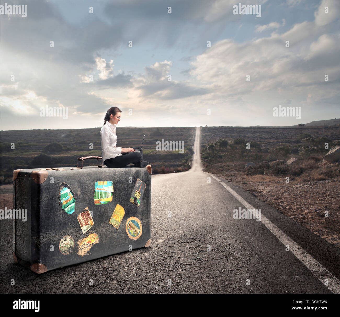 Femme assise sur une valise géante sur le long chemin Photo Stock - Alamy