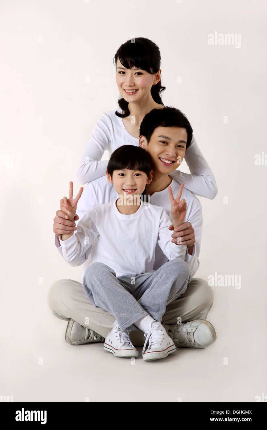 La famille de l'Asie de l'est avec un enfant assis en ligne sur le plancher avec sourire, regardant la caméra Banque D'Images