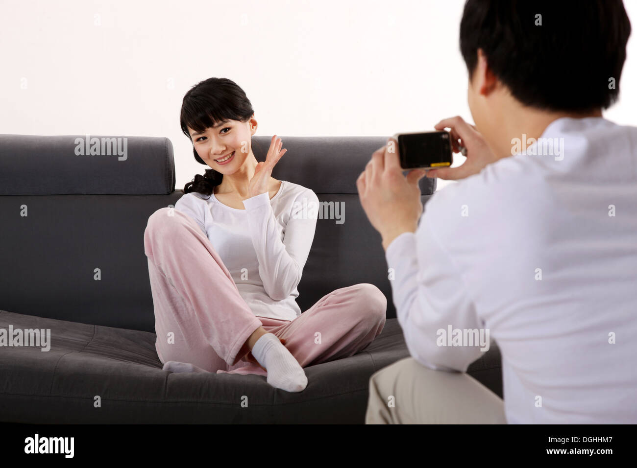 East Asian couple dans des vêtements blancs, l'homme de prendre photo de la femme assise sur le canapé Banque D'Images