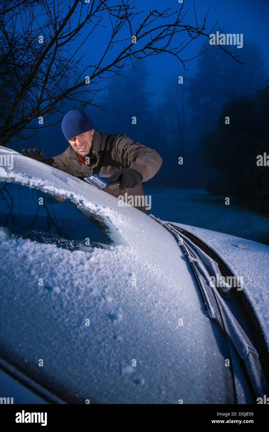 Homme racler la glace d'une voiture couverte de givre pare brise. Banque D'Images