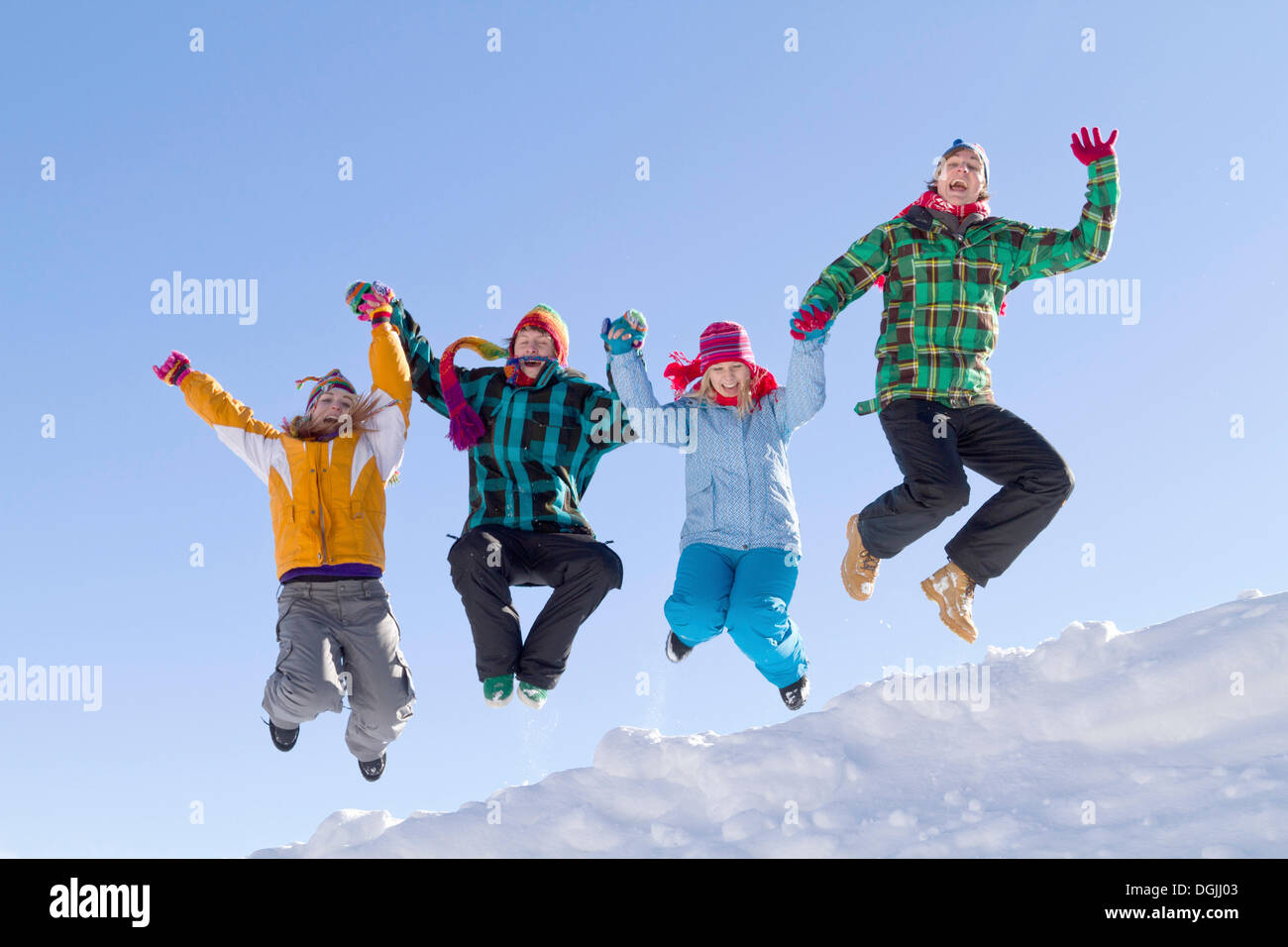 Quatre jeunes gens portant des vêtements d'hiver coloré sautant par dessus une crête couverte de neige, Flachau, Salzbourg, Autriche, Europe Banque D'Images