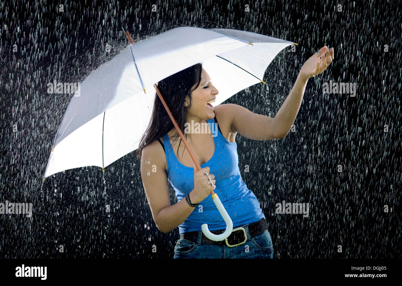 Jeune femme indienne tenant un parapluie blanc tout en profitant de la pluie avec extase Banque D'Images