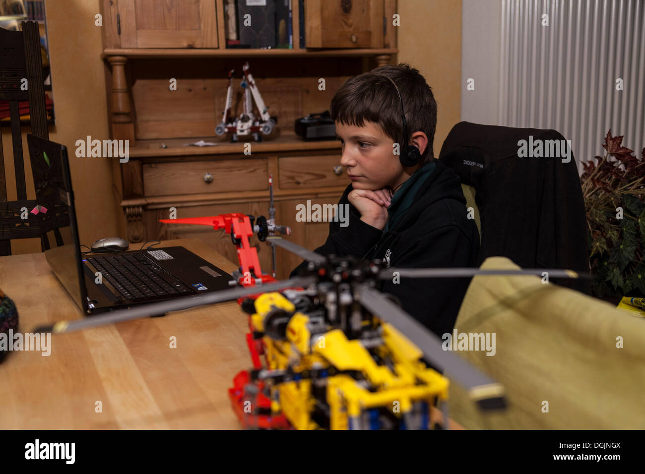 Garçon, 12 ans, regarder des vidéos sur un ordinateur portable avec des écouteurs, en face d'un jeu de construction Lego Banque D'Images