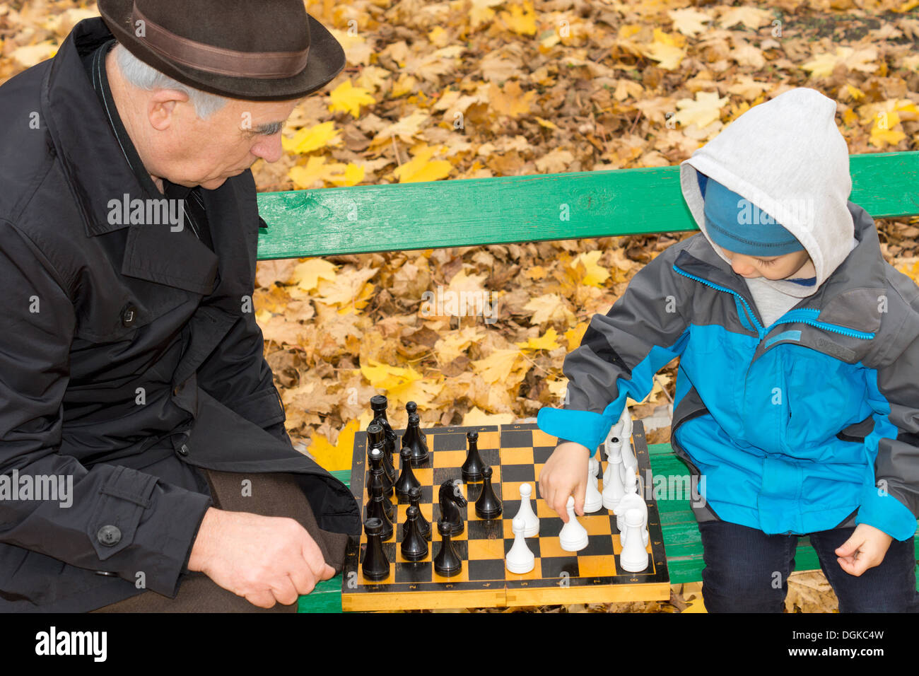 Grand-père âgé assis sur un banc de parc en bois à l'extérieur à l'automne d'enseigner son mignon petit-fils à jouer aux échecs Banque D'Images
