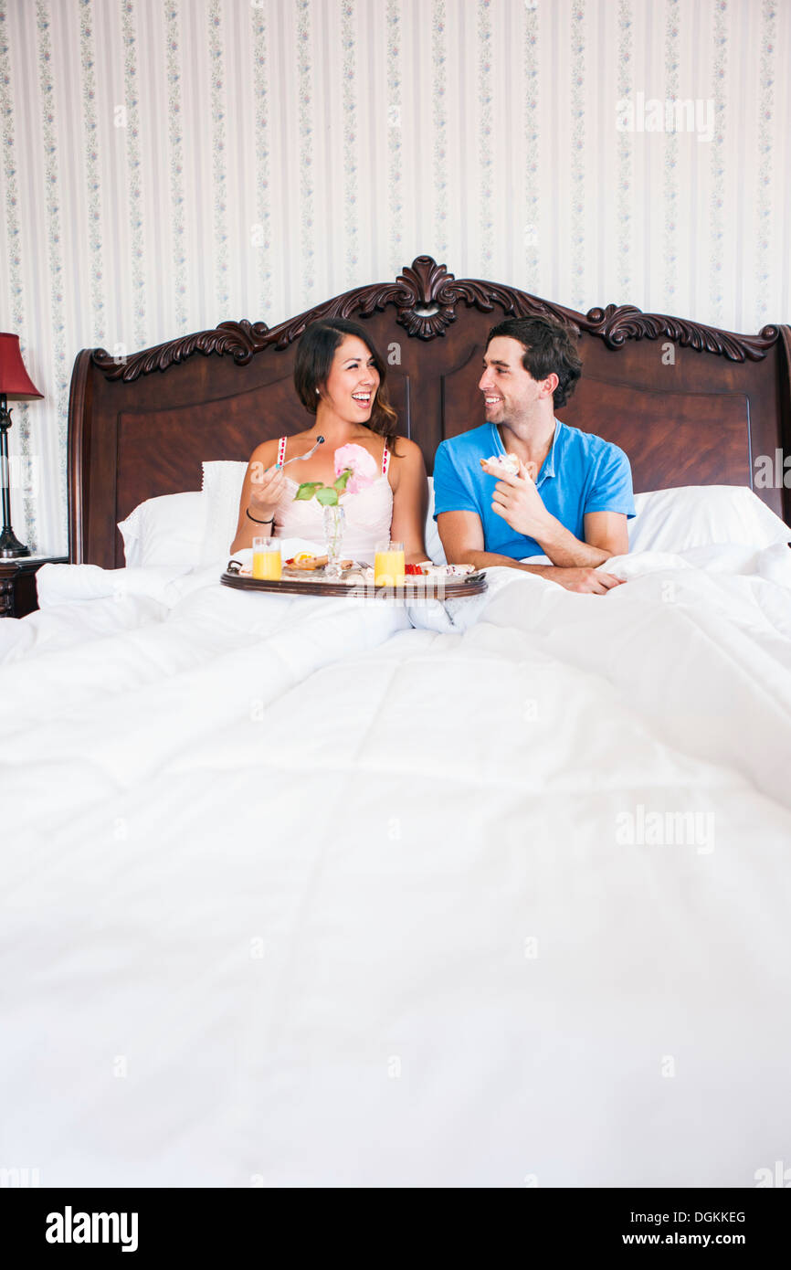 Jeune couple eating breakfast in bed in hotel room Banque D'Images