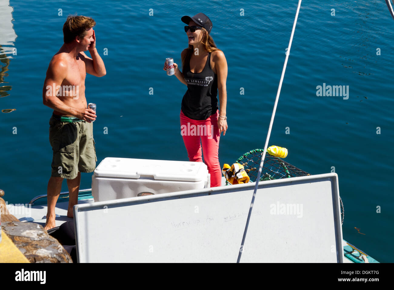 Jeune homme et femme bénéficiant d'une bière et d'un rire tout en se tenant sur un bateau amarré dans le port de Santa Barbara, en Californie. Banque D'Images