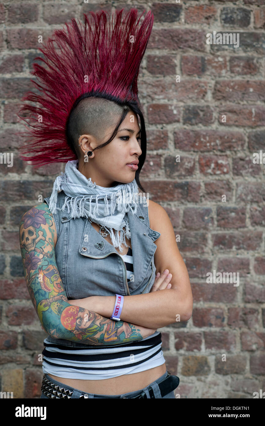 Une jeune femme avec bras tatoués et Mohican rouge style de cheveux pose pour la caméra à la London International Convention de tatouage. Banque D'Images