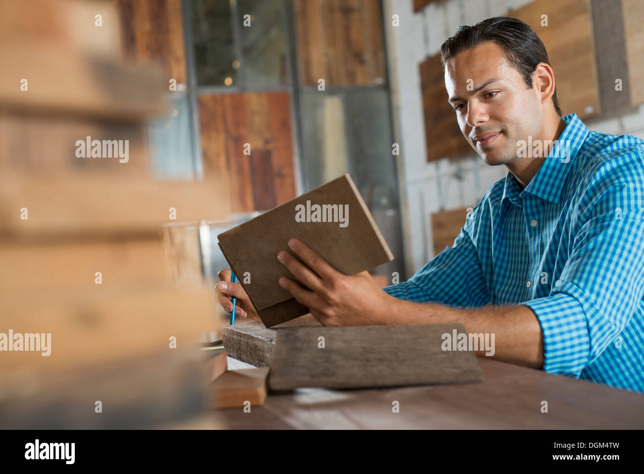 Un jeune homme dans un atelier de l'examen d'un échantillon de bois recyclé. Banque D'Images