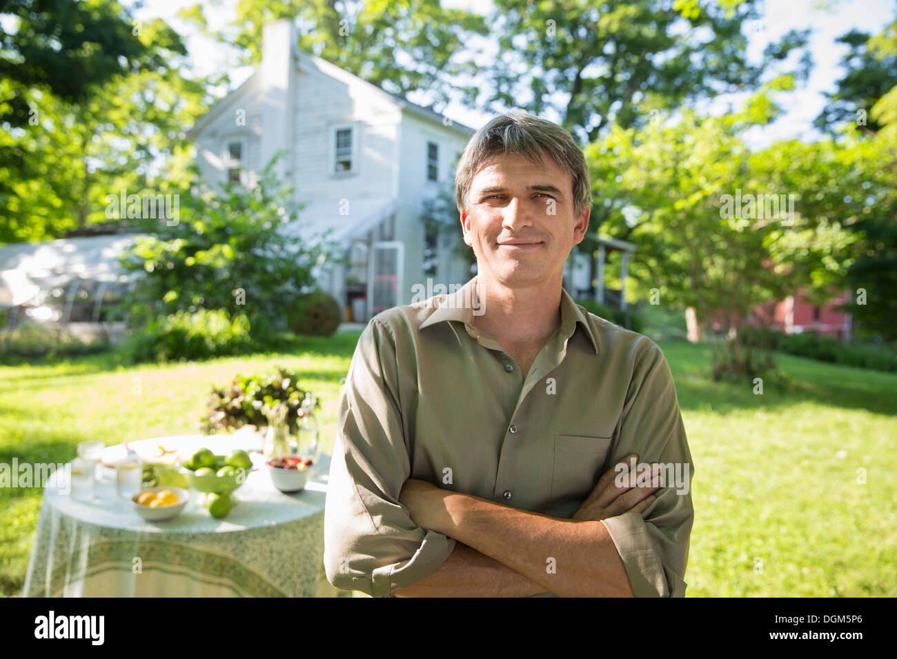 À la ferme. Un homme dans un corps de ferme, jardin à côté d'une table ronde avec un verre de limonade fraîche. Banque D'Images