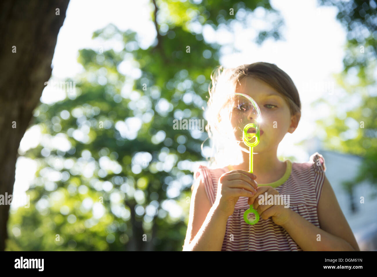 L'extérieur en été. Une jeune fille faisant des bulles dans l'air sous les branches d'un gros arbre. Banque D'Images