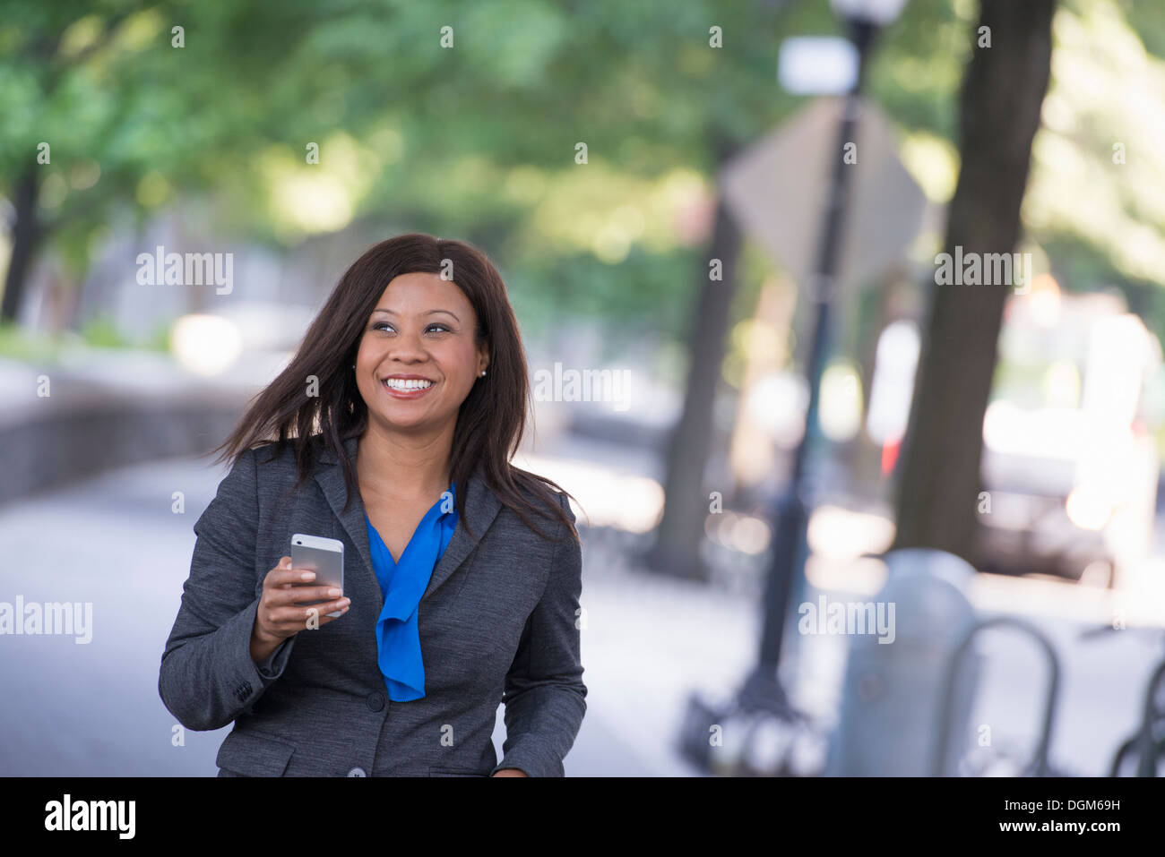 L'été. Une femme dans un costume gris avec une chemise bleu vif. La tenue d'un téléphone intelligent. Banque D'Images