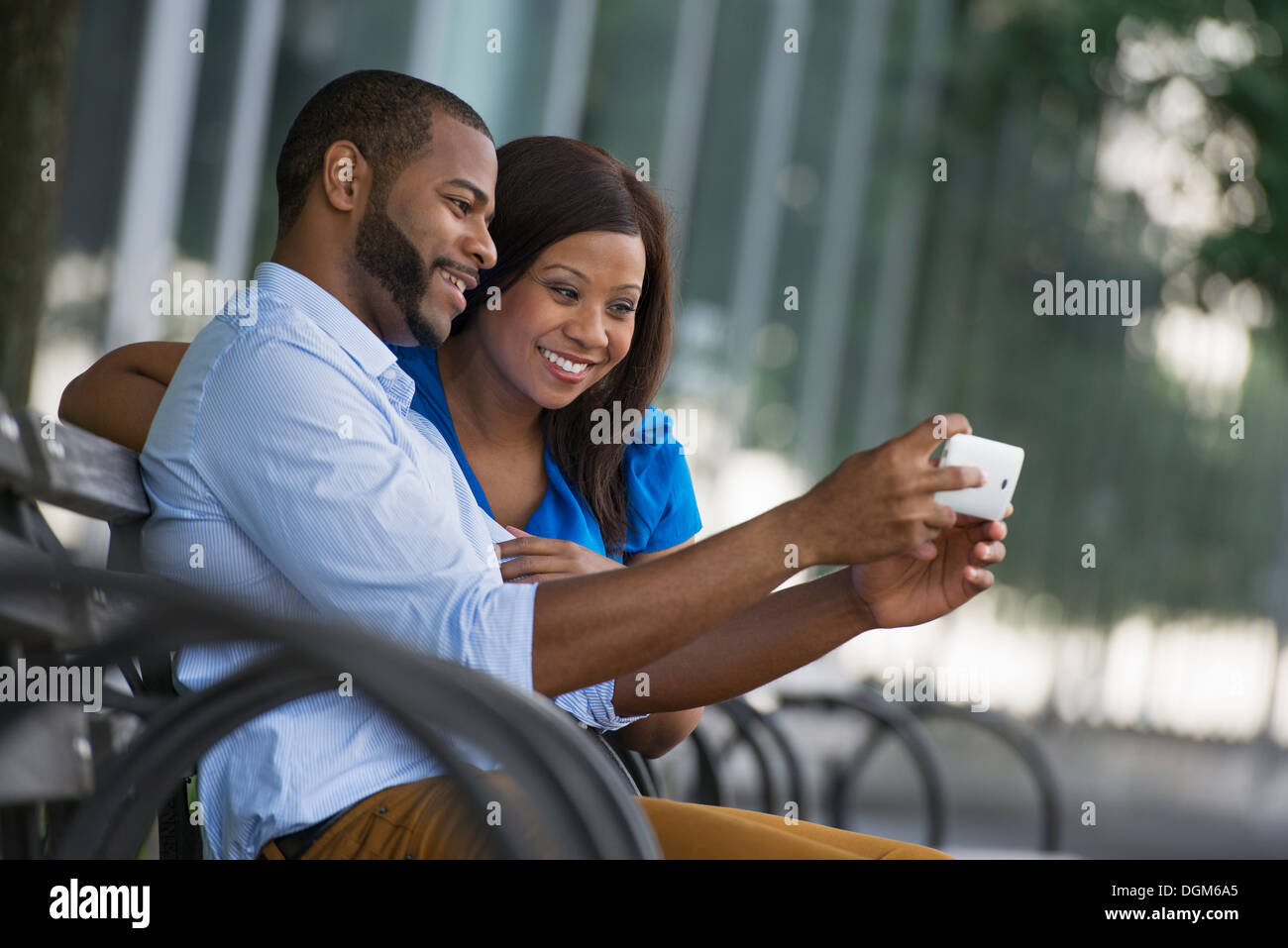 L'été. Un couple assis sur un banc, prenant une photographie selfy. Banque D'Images