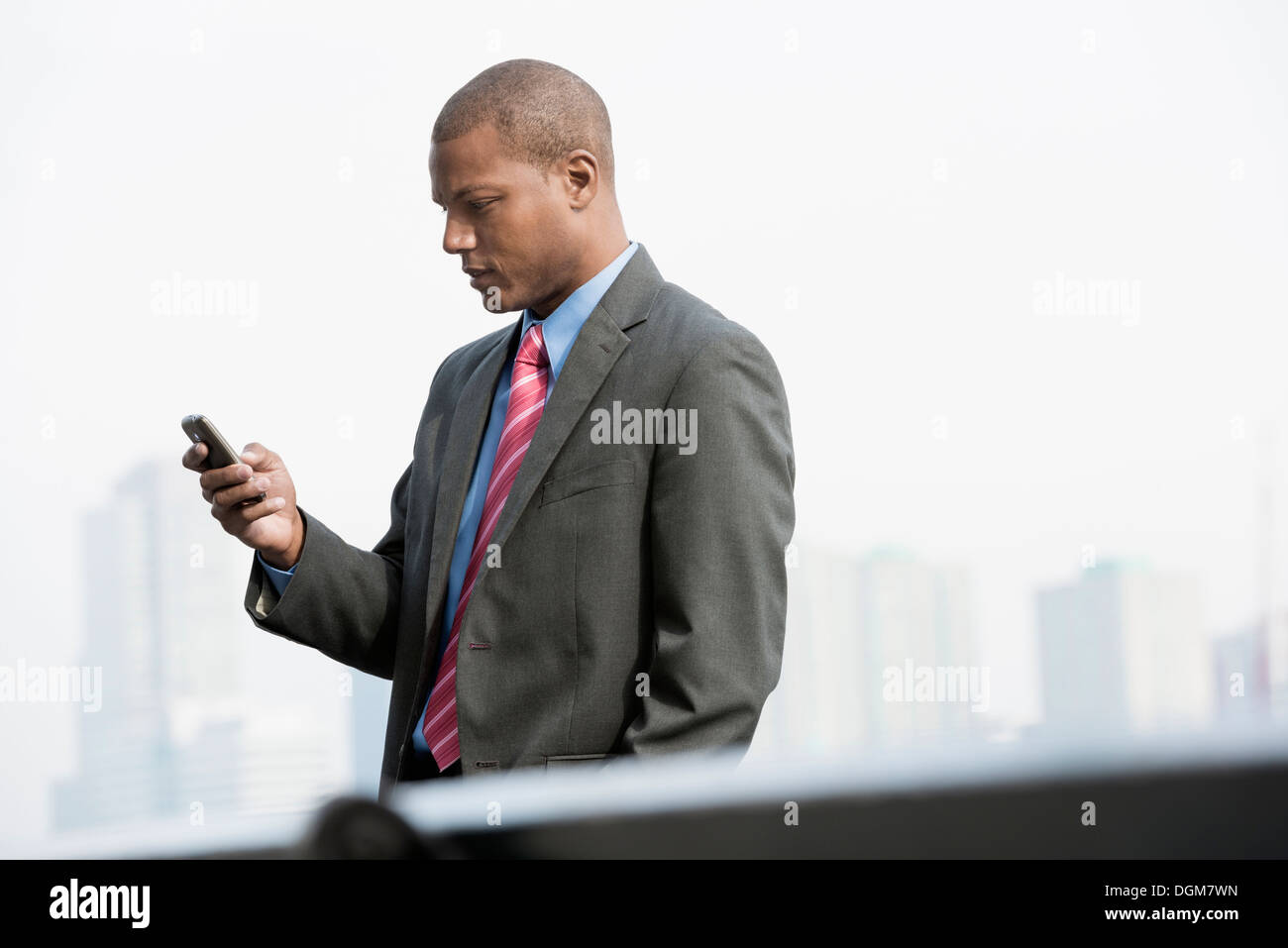 Un jeune homme dans un costume avec une chemise bleue et cravate rouge. Sur une rue de la ville de New York. À l'aide d'un téléphone intelligent. Banque D'Images