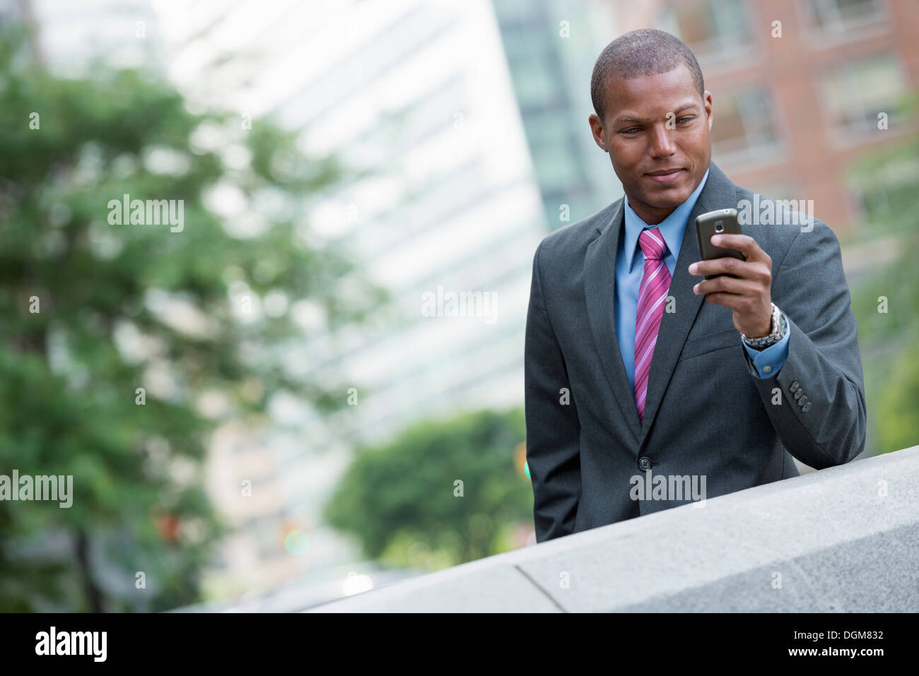 Un jeune homme dans un costume avec une chemise bleue et cravate rouge. Sur une rue de la ville de New York. À l'aide d'un téléphone intelligent. Banque D'Images