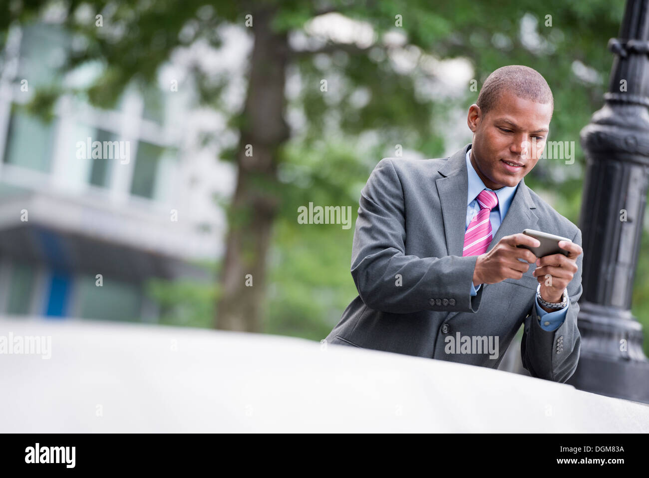 Un jeune homme dans un costume avec une chemise bleue et cravate rouge. Sur une rue de la ville de New York. À l'aide d'un téléphone intelligent. Banque D'Images