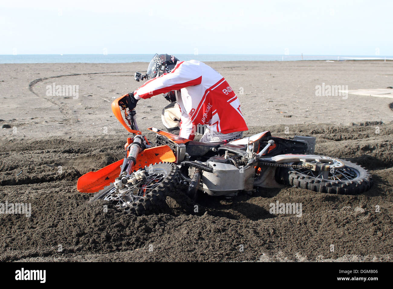 Un pilote de motocross falls avec son vélo sur le sable près de la mer Banque D'Images