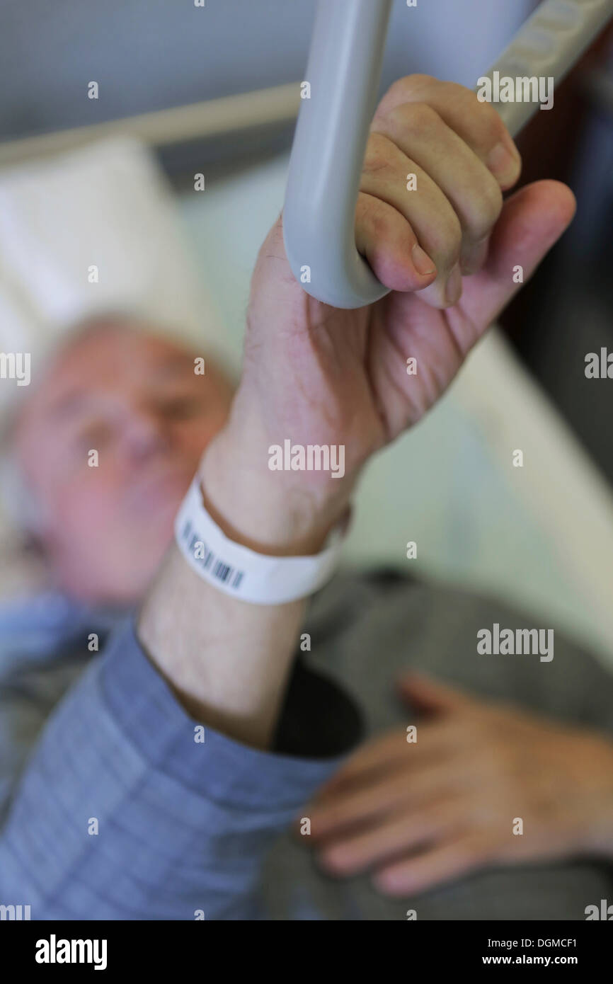 Un homme âgé dans un hôpital, main tenant une poignée dans un lit d'hôpital Banque D'Images