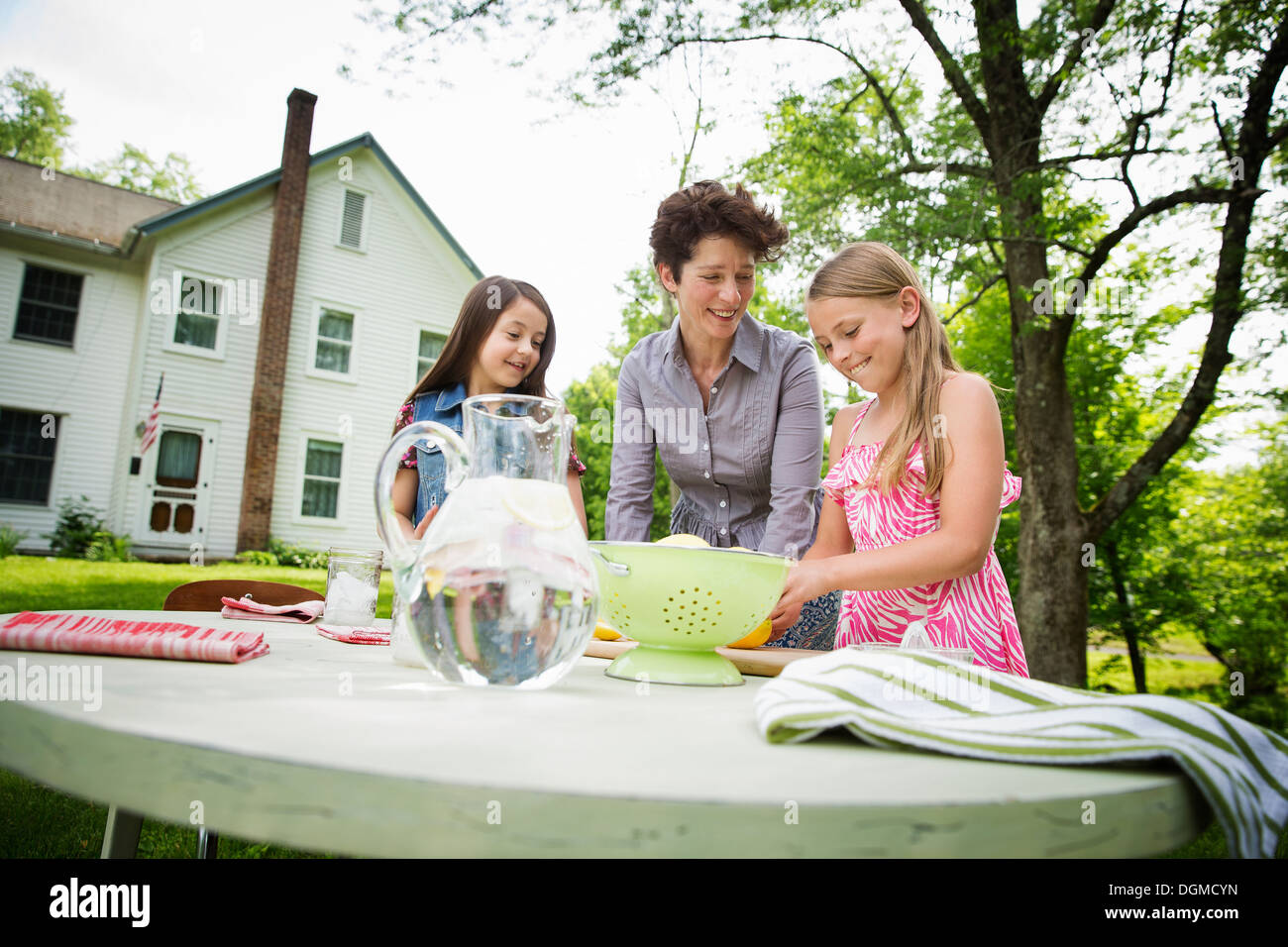 Une réunion de famille d'été dans une ferme. Une femme et deux enfants à l'extérieur par une table, fixant la table. Faire de la limonade. Banque D'Images