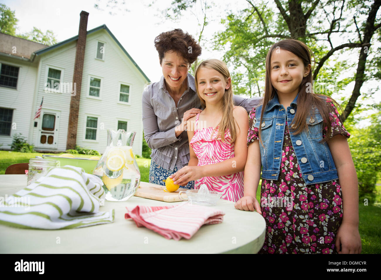 Une réunion de famille d'été dans une ferme. Une femme et deux enfants à l'extérieur par une table, fixant la table. Faire de la limonade. Banque D'Images