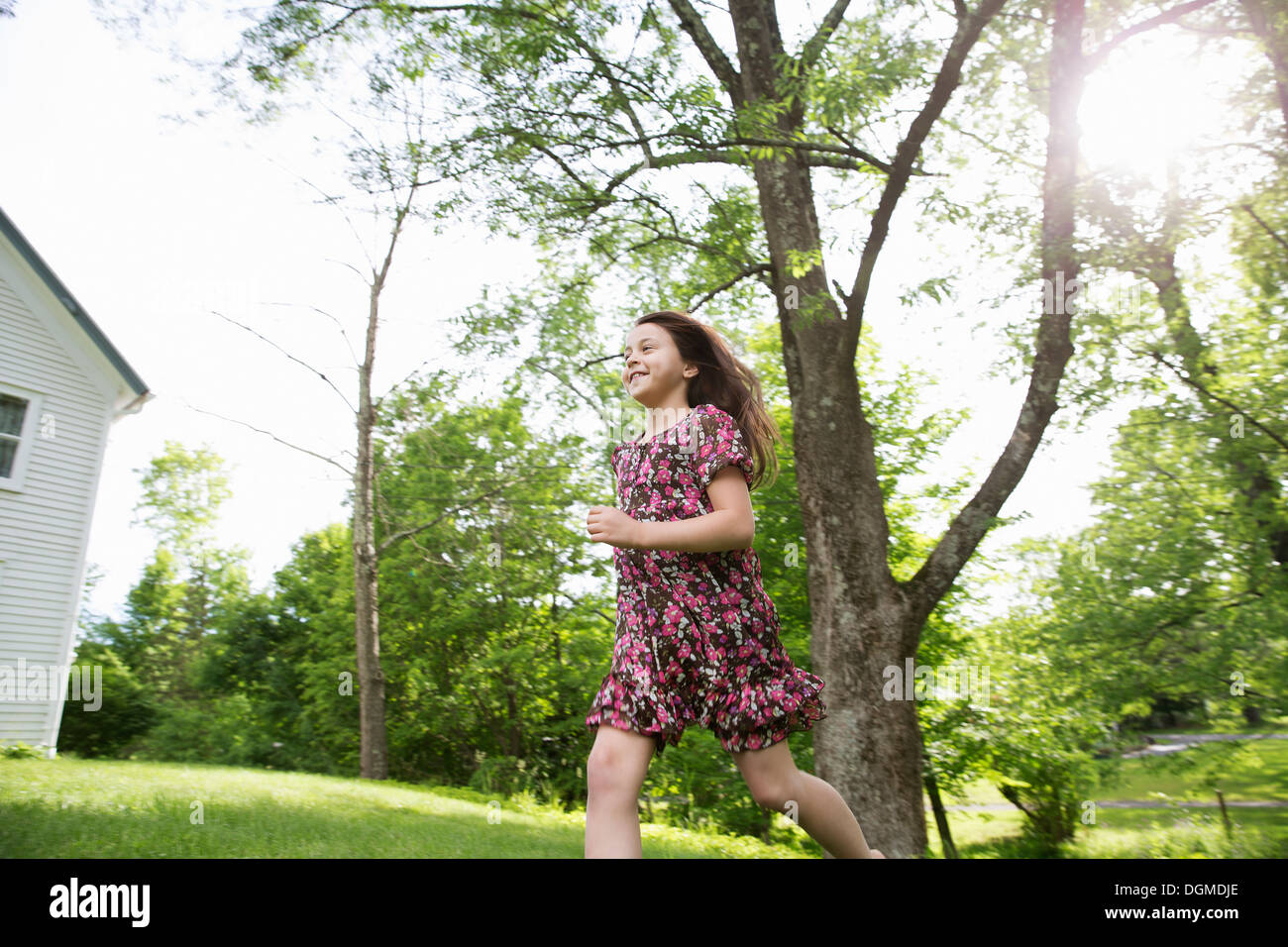 Une jeune fille dans une robe à motifs, courir sur l'herbe à l'ombre des arbres dans un jardin de ferme. Banque D'Images