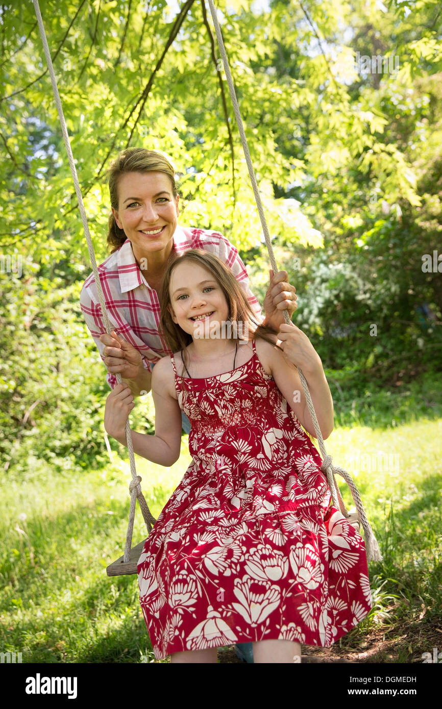 L'été. Une fille dans une robe d'été sur une balançoire accrochée à une branche d'arbre. Une femme mature derrière elle. Banque D'Images