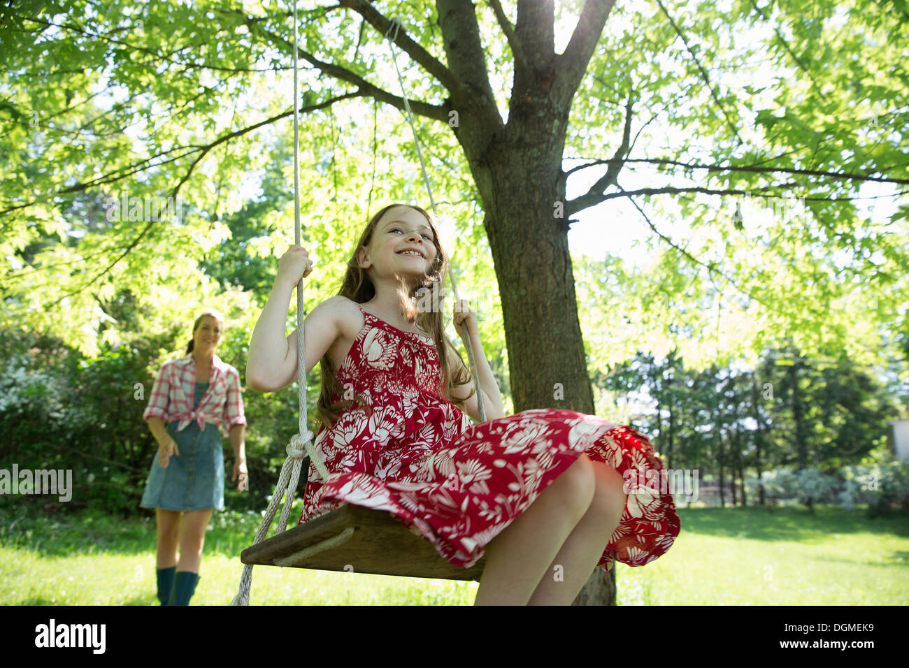 L'été. Une fille dans une robe d'été sur une balançoire accrochée à une branche d'arbre. Une femme derrière elle. Banque D'Images
